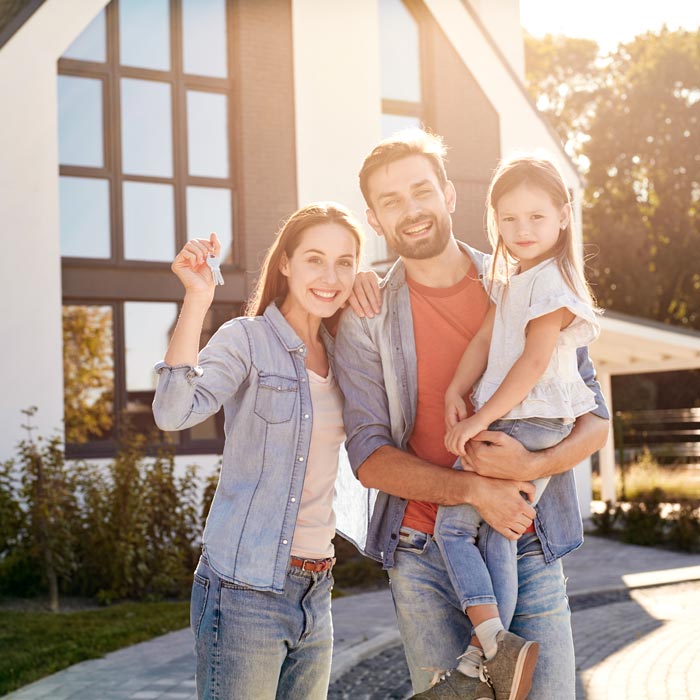 Family of three standing outdoors holding keys to new apartment